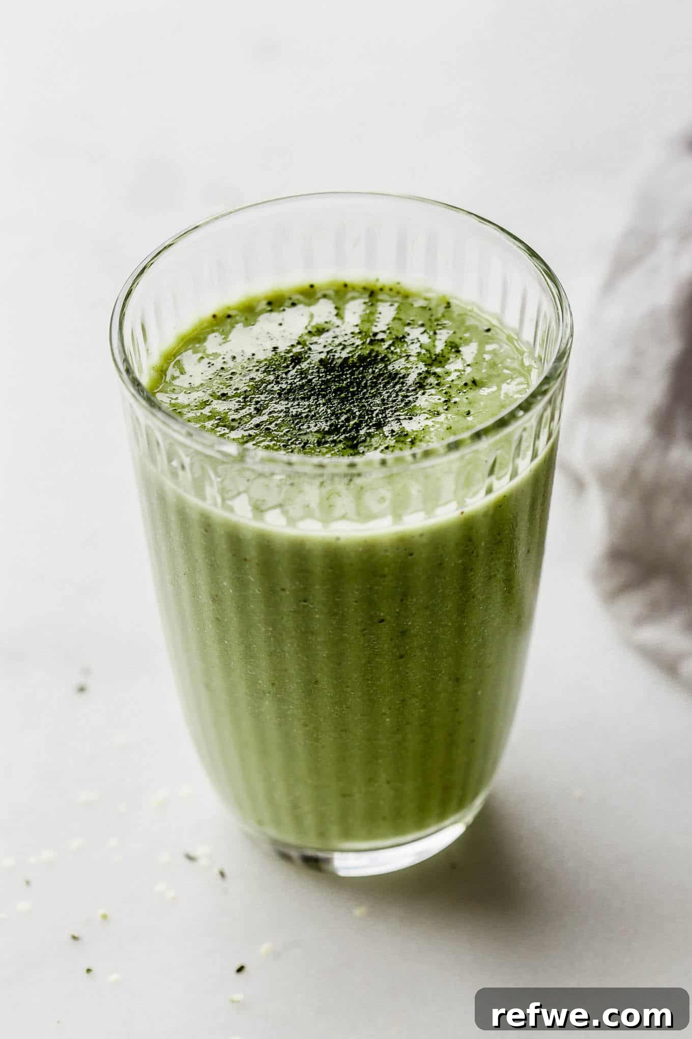 Vibrant Matcha Smoothie 7 A close-up of a single glass of matcha green tea smoothie, beautifully topped with a dusting of matcha powder, on a light background.