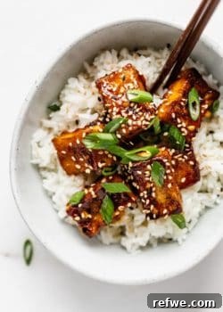 A top-down view of a bowl of crispy orange tofu served with rice and garnished with green onions and sesame seeds.