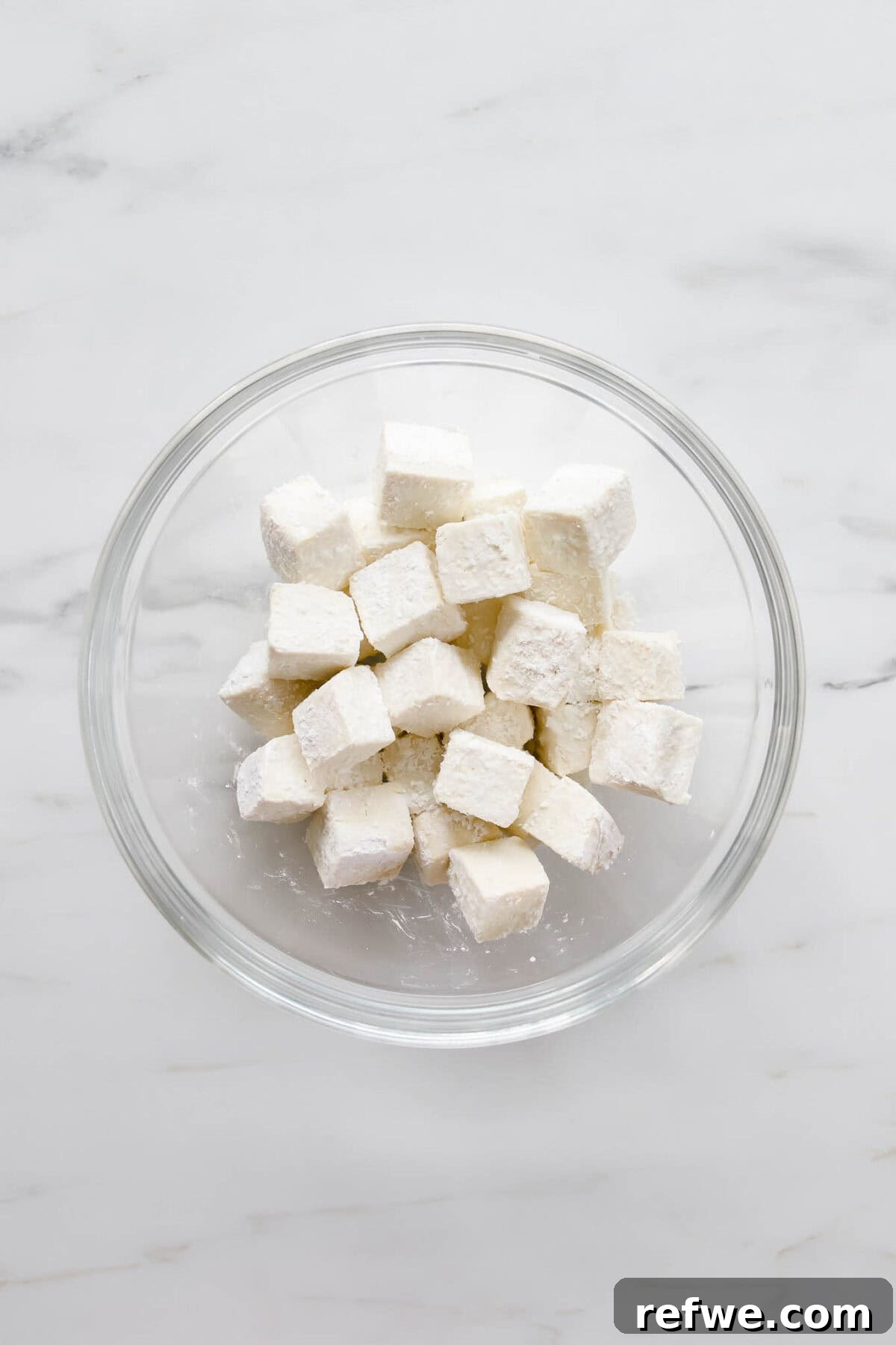 Zesty Crispy Tofu Sheet Pan Delight 4 Tofu cubes evenly coated in cornstarch in a glass bowl.