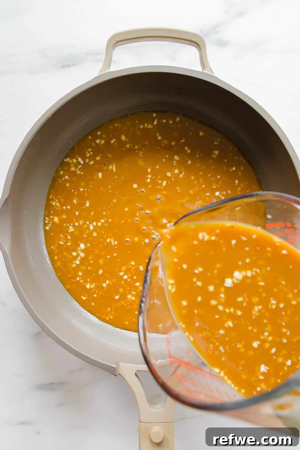 Zesty Crispy Tofu Sheet Pan Delight 6 Rich orange sauce being poured into a pan, ready to simmer.