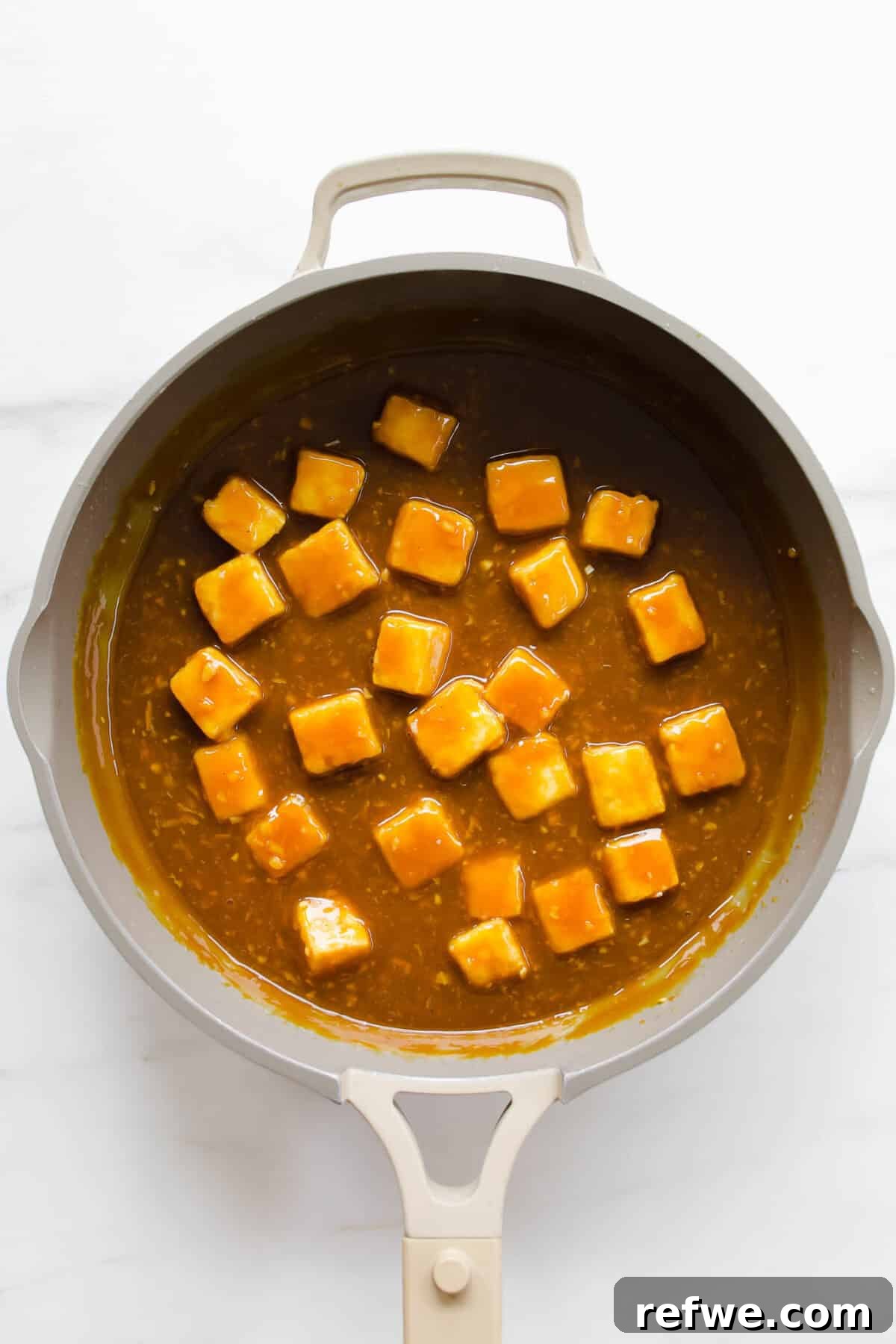 Zesty Crispy Tofu Sheet Pan Delight 7 Crispy orange tofu being tossed in a pan with the thickened sauce, coating each piece.