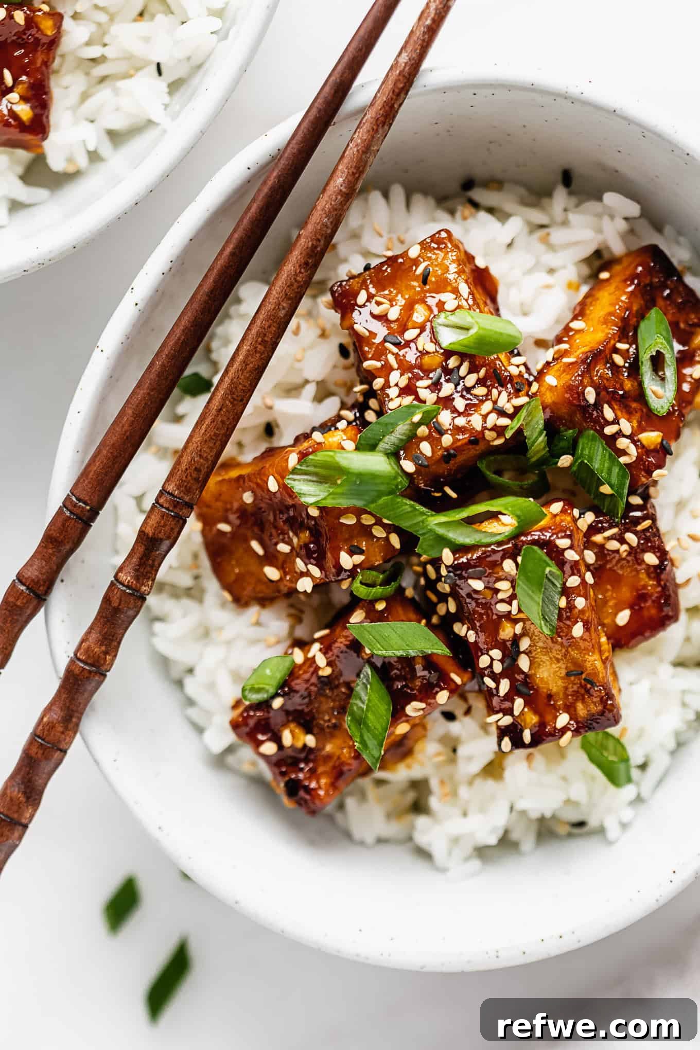 Zesty Crispy Tofu Sheet Pan Delight 8 A beautifully plated bowl of crispy orange tofu served over white rice, garnished with fresh scallions and sesame seeds.