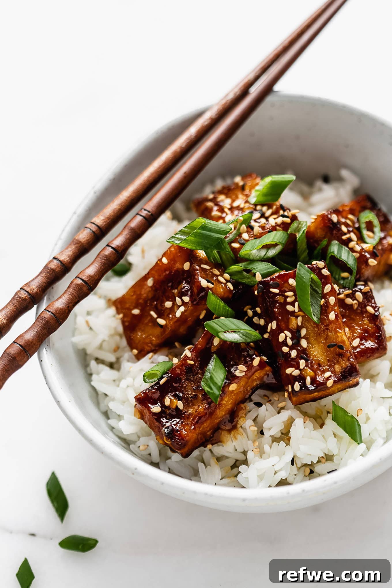 Zesty Crispy Tofu Sheet Pan Delight 9 A tantalizing close-up of a bowl of crispy orange tofu and rice with chopsticks, inviting you to take a bite.