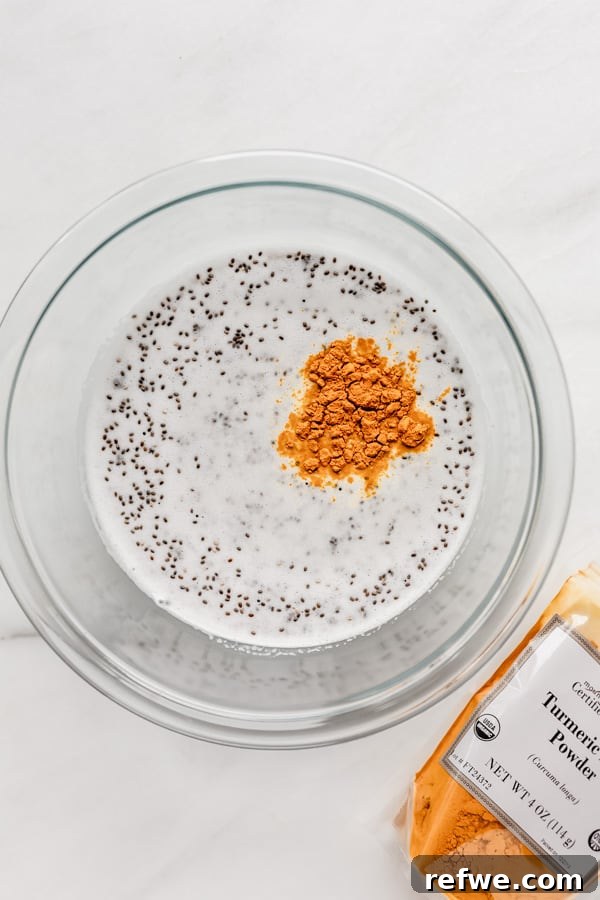 Golden Glow Chia Pudding 5 A clear mixing bowl containing rich coconut milk, raw chia seeds, and vibrant turmeric powder, ready to be combined.