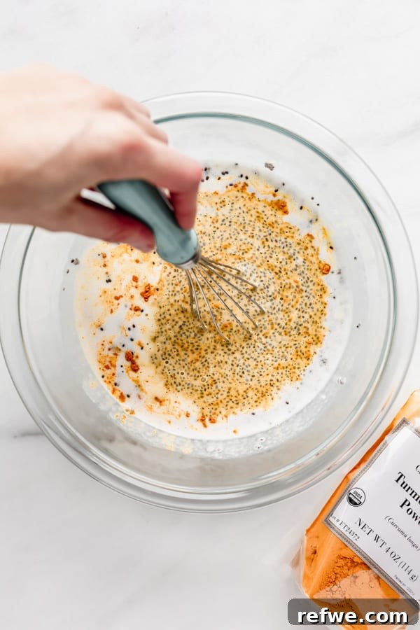 Golden Glow Chia Pudding 6 A hand actively whisking the mixture of chia seeds, coconut milk, and turmeric in a clear mixing bowl, illustrating the combining process.
