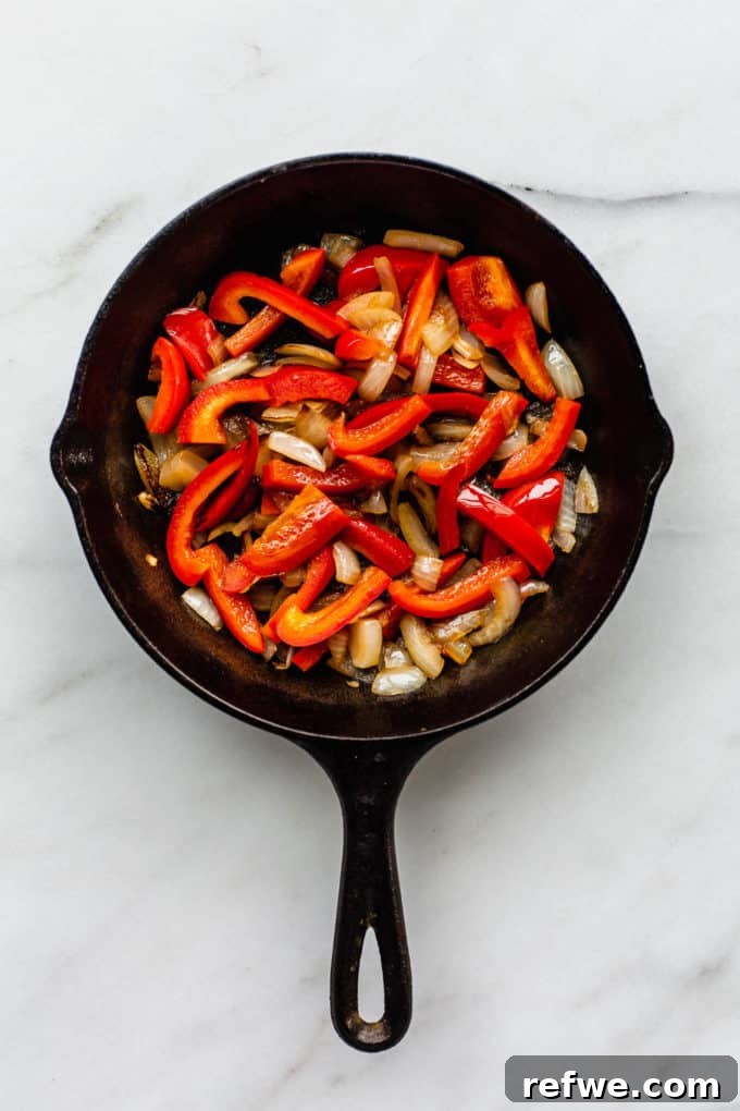 Hearty Vegan Shakshuka 3 Sliced red peppers and onions sautéing in a cast iron skillet, forming the flavorful aromatic base for the vegan shakshuka.