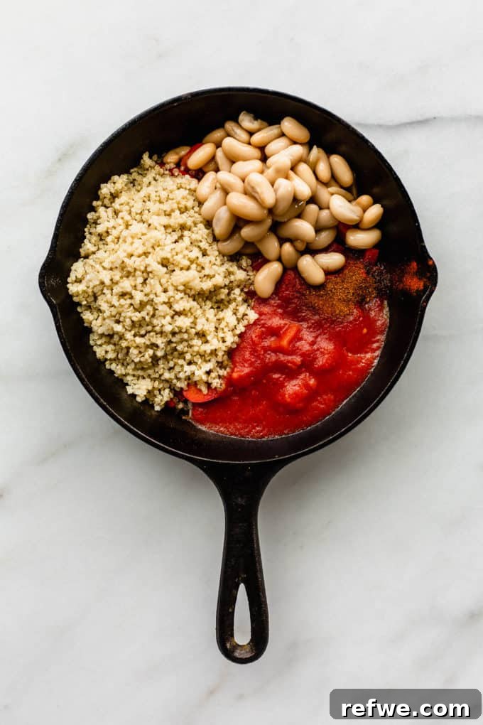 Hearty Vegan Shakshuka 4 A cast iron skillet generously filled with vibrant red peppers, rich crushed tomatoes, creamy white beans, and wholesome quinoa, ready to simmer and meld flavors.