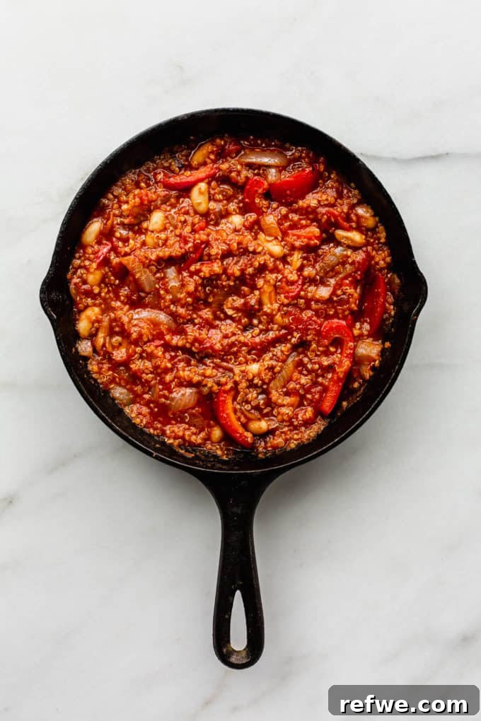 Hearty Vegan Shakshuka 6 A close-up view of the wholesome quinoa, rich crushed tomatoes, vibrant red peppers, and creamy white beans simmering together in a cast iron skillet, developing profound, melded flavors.