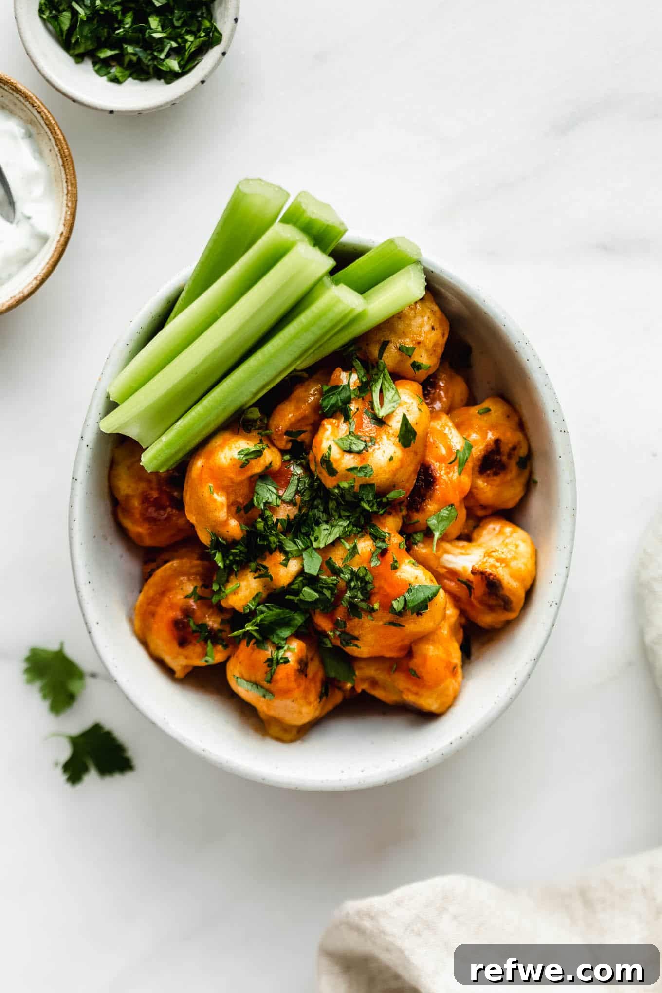 Buffalo Cauliflower Bites 2 A bowl of freshly baked Buffalo Cauliflower Wings garnished with celery sticks, ready to be served.