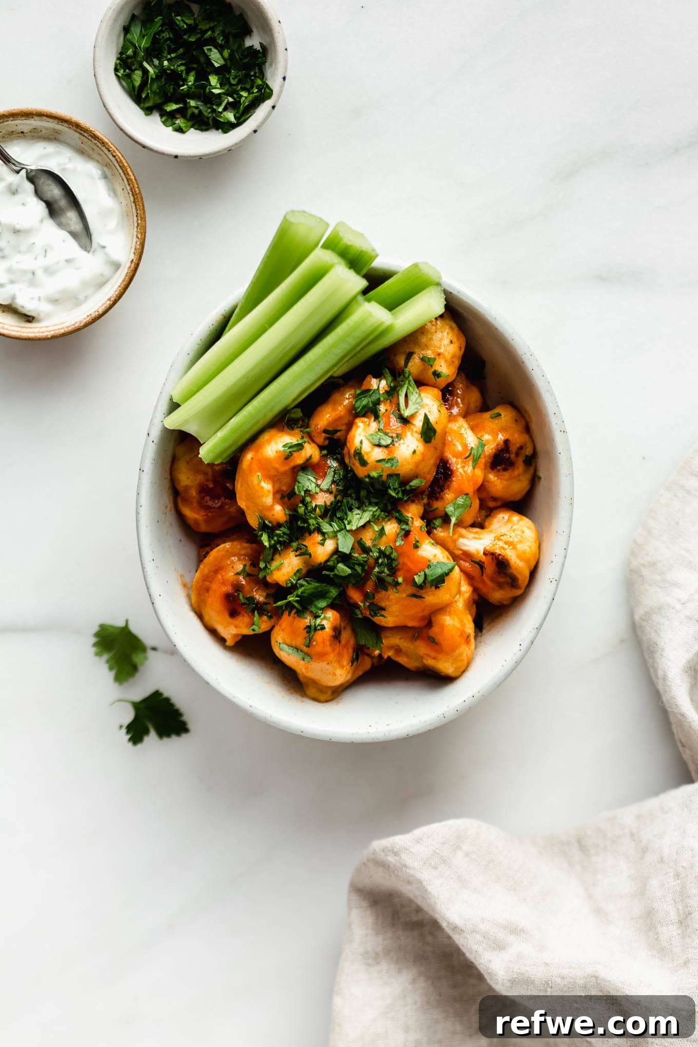 Buffalo Cauliflower Bites 7 A delightful bowl of Buffalo Cauliflower Wings, with a side of fresh celery sticks and a napkin, inviting a delicious snack.