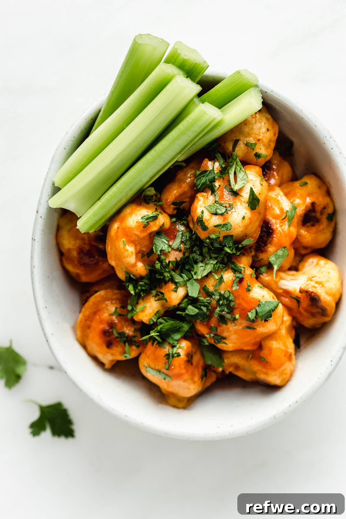 Buffalo Cauliflower Bites 8 A beautifully presented bowl of Buffalo Cauliflower Wings, with fresh celery sticks and a dipping sauce, ready to be enjoyed.