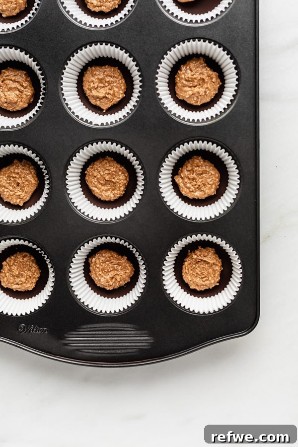 Decadent Dark Chocolate Almond Butter Delights 5 A muffin pan filled with muffin liners, a layer of set chocolate, and a scoop of almond butter filling on top.