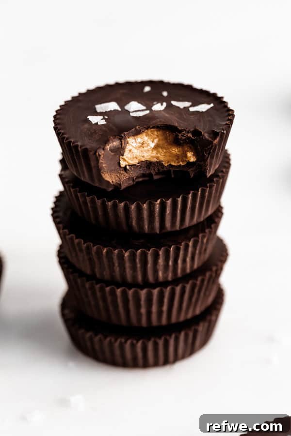Decadent Dark Chocolate Almond Butter Delights 7 A stack of five dark chocolate almond butter cups, topped with flaky sea salt, beautifully presented.