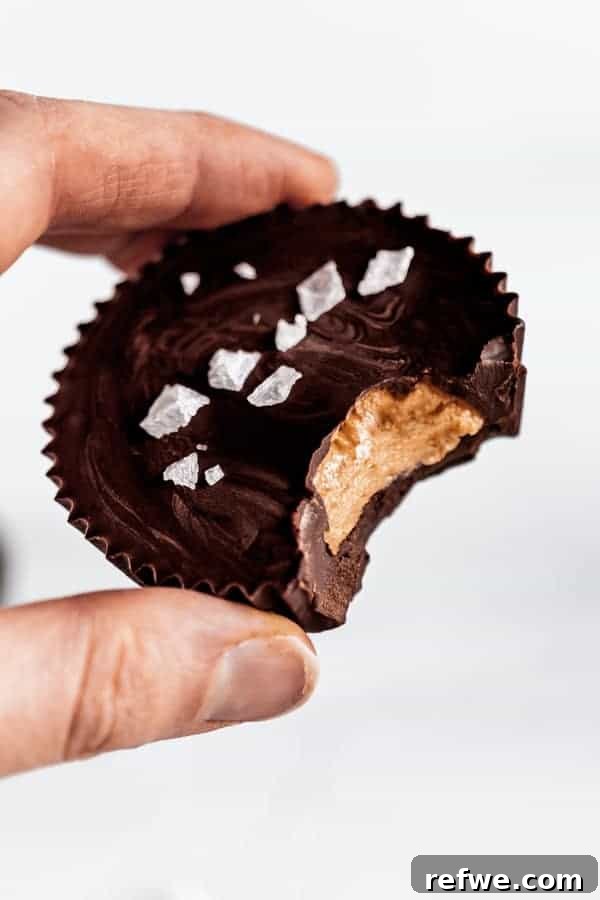 Decadent Dark Chocolate Almond Butter Delights 8 A hand holding a dark chocolate almond butter cup with a bite taken out of it, showing the soft, delicious almond butter center.