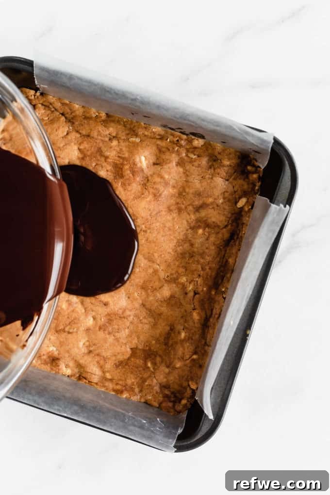 Decadent Chocolate Peanut Butter Muscle Bars 8 Melted dark chocolate being poured over the pressed protein bar base in the pan.