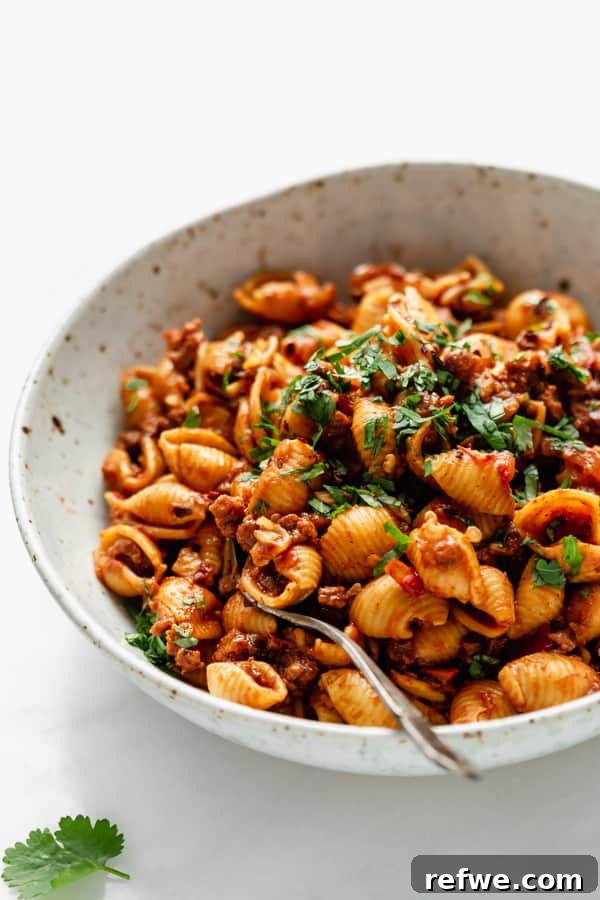 Zesty Plant-Based Taco Pasta 8 A close-up shot of perfectly cooked shell noodles generously coated in a rich, vibrant vegan taco pasta sauce, served in a white speckled bowl.