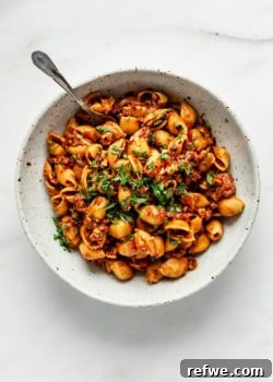 A top-down view of a white speckled pasta bowl filled with vegan taco pasta, garnished with fresh cilantro.