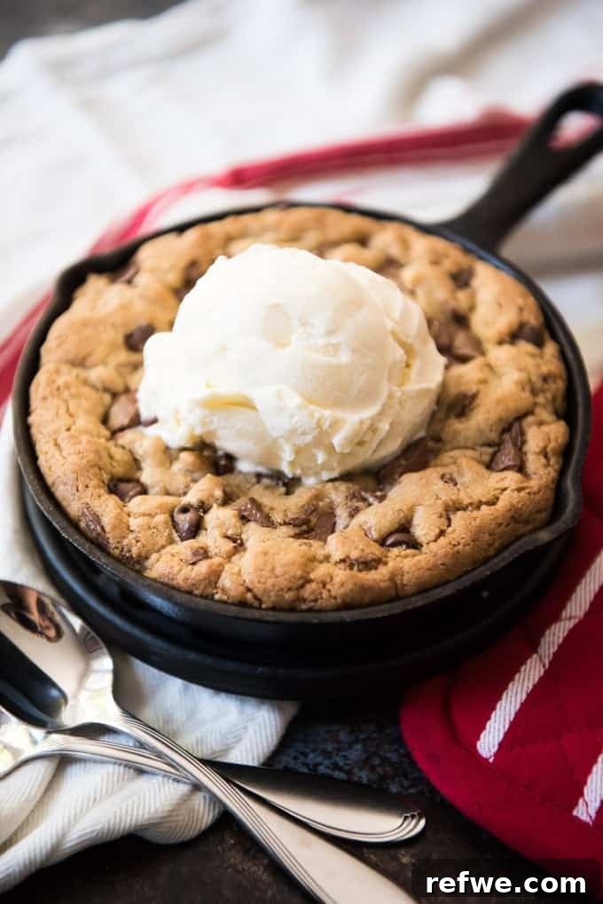 Effortless Elegance: 20 Stunning Date Night Dinners 16 A single cast iron chocolate chip cookie skillet, warm and gooey, topped with a scoop of melting vanilla ice cream and two silver spoons, resting on a red oven mitt and white linen on a black countertop, ideal for sharing.