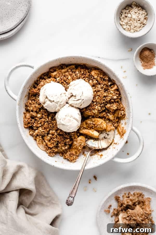 Effortless Elegance: 20 Stunning Date Night Dinners 18 A silver serving spatula under a generous portion of healthy apple crisp in a white baking dish, topped with three scoops of ice cream and surrounded by oats and brown sugar on a tan linen.