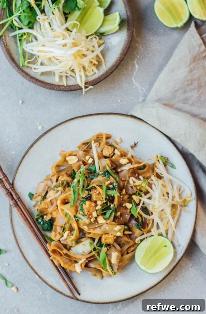 Hearty Vegan Pad See Ew 4 A generously portioned plate of Vegan Pad See Ew, garnished with chopped green onions, crushed peanuts, and a fresh lime wedge, ready to be squeezed.