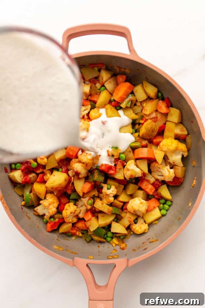 Smooth cashew cream being poured into the pan of cooked vegetables and spices.