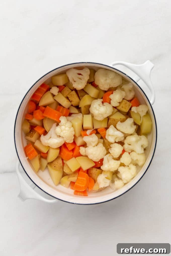 Chopped cauliflower, potatoes, and carrots in a pot of water, ready for par-boiling.