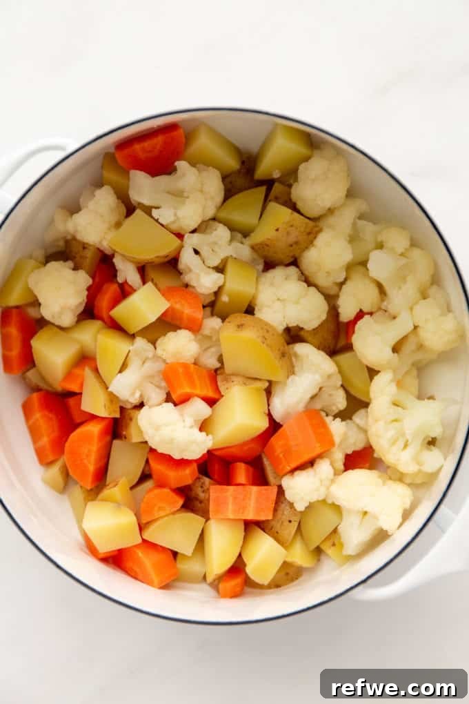 Steamed potatoes, carrots, and cauliflower in a white pot, partially cooked.