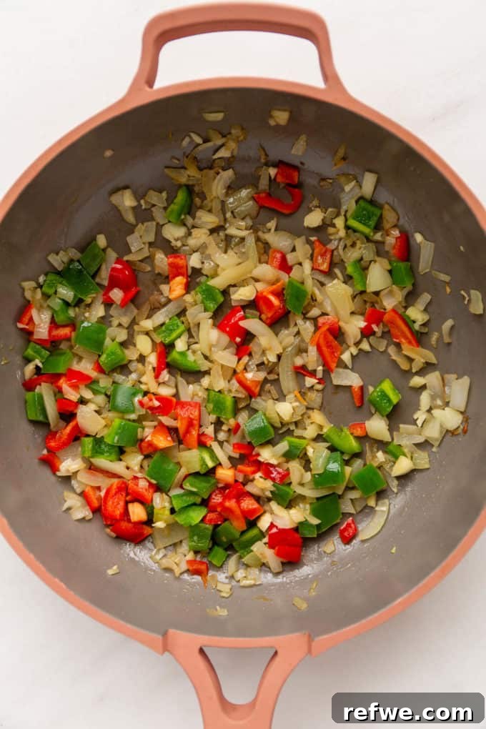 Sautéing chopped bell peppers and onions in a pan for the curry base.