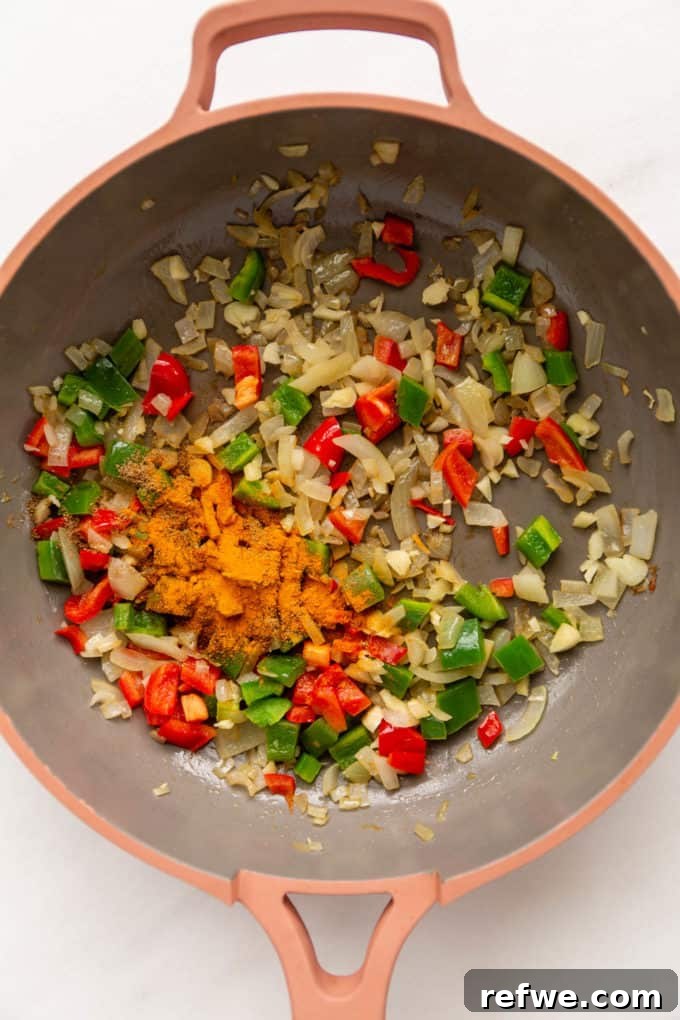 Sautéed bell peppers and onions in a pan, now with added aromatic spices.