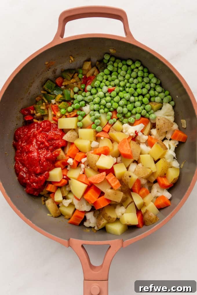 Vegetables, frozen peas, and crushed tomatoes combined in a pan, stirring.