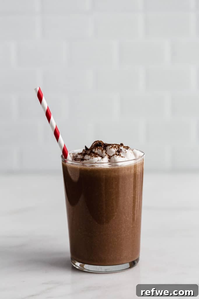 Blended Cocoa Chill 4 A close-up shot of frozen hot chocolate in a glass, topped with a generous swirl of coconut whipped cream and delicate chocolate shavings.