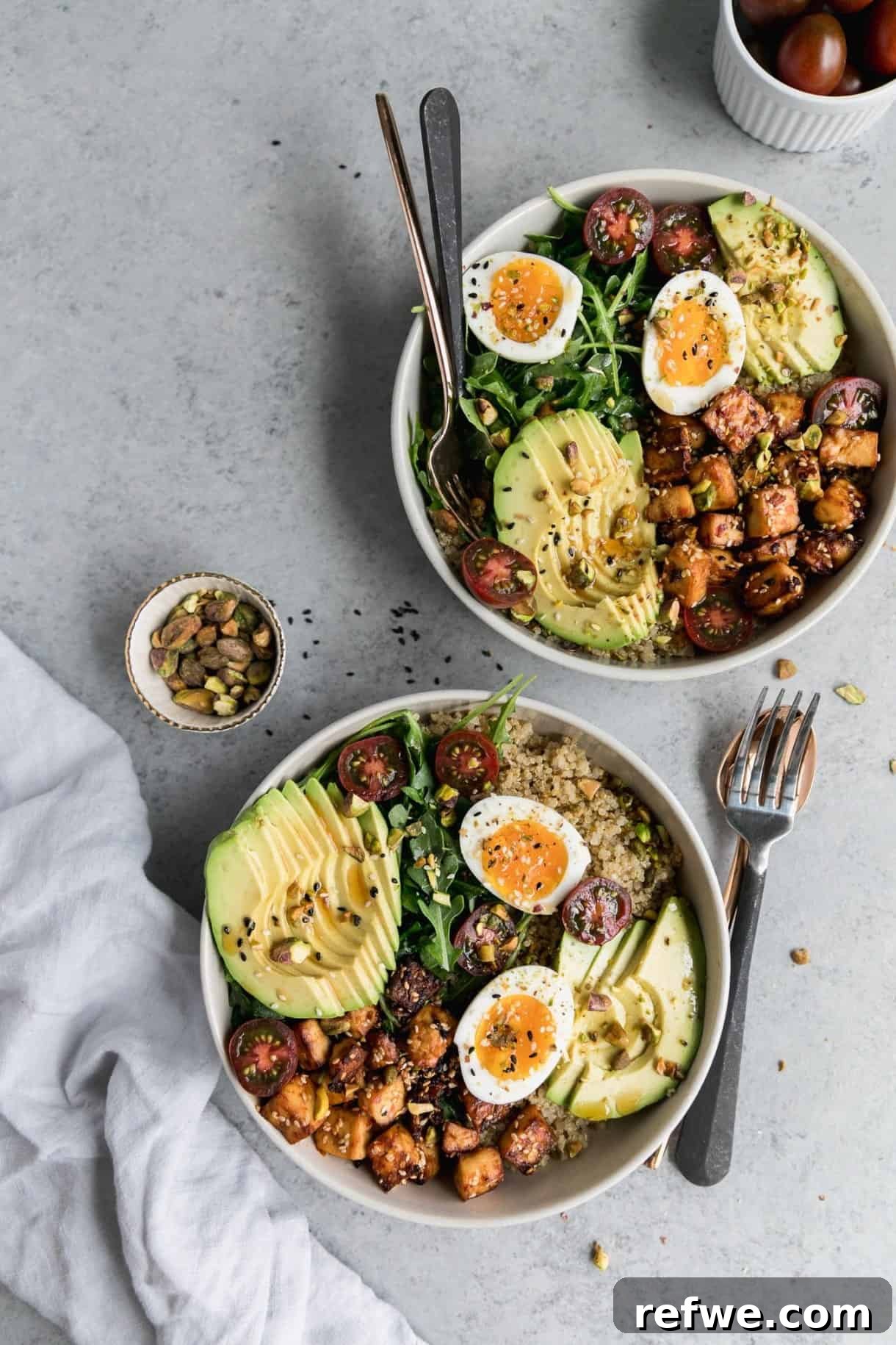 A satisfying quinoa bowl featuring perfectly cooked eggs, savory sesame tofu, creamy avocado slices, and fresh arugula.