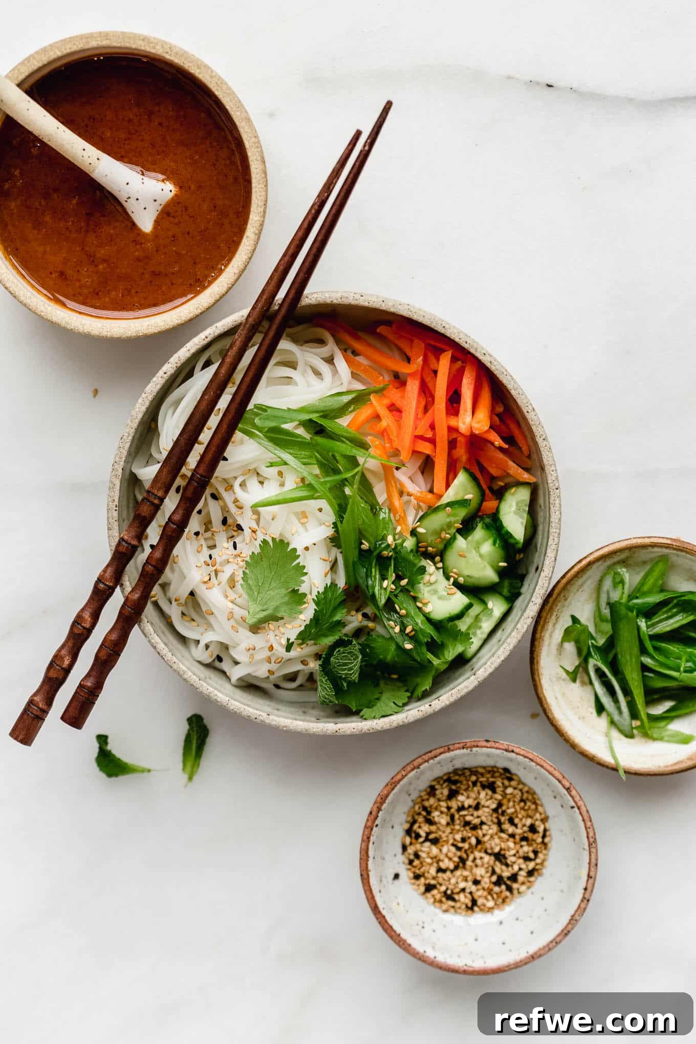A vibrant spring roll noodle bowl featuring delicate rice noodles, crispy tofu, and a side of rich almond butter sauce.