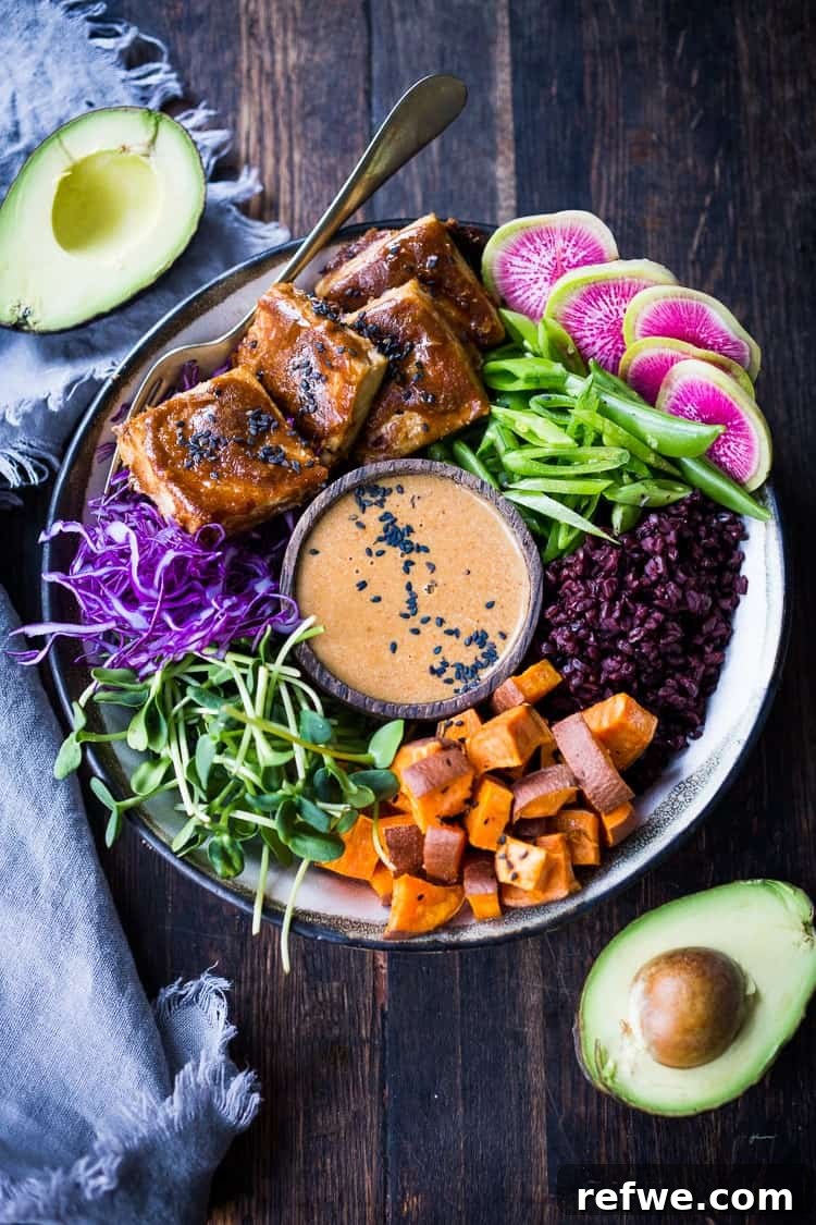 A vibrant Bali bowl featuring rich peanut sauce in a central wooden dish, surrounded by crispy peanut tofu, shredded cabbage, microgreens, and sweet potatoes.