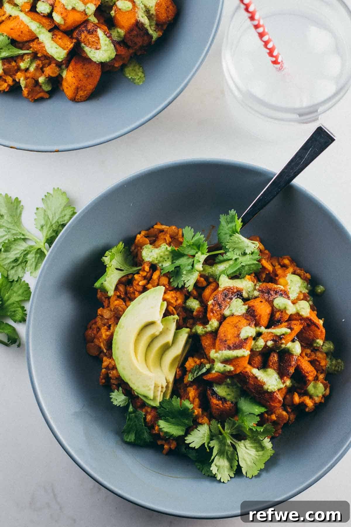Creamy sliced avocado atop a rich lentil curry served in a blue bowl, garnished with fresh green cilantro, creating a vibrant and comforting dish.