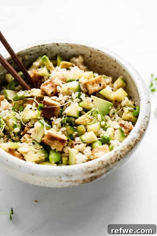 A mixed vegan poke bowl with rice, vegetables, and crispy tofu, featuring chopsticks resting on the side, ready to eat.