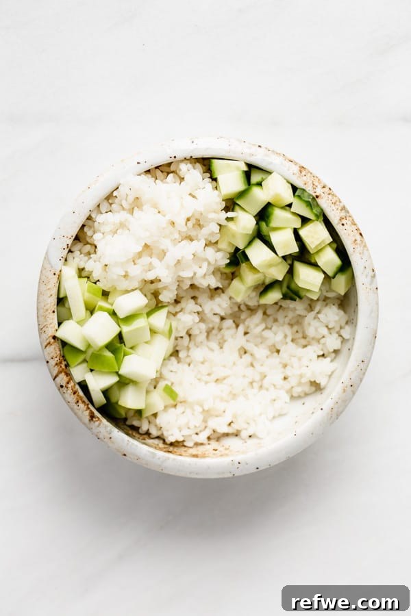 A bowl of rice and cucumber with added cubes of fresh green apple.