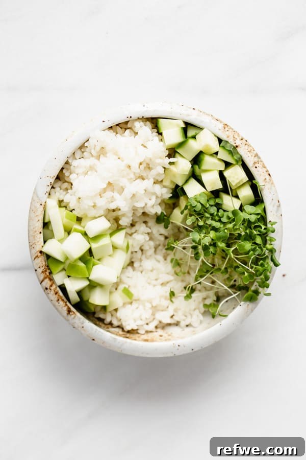 A poke bowl in progress, featuring rice, cucumber, apple, and a vibrant pile of green sprouts.