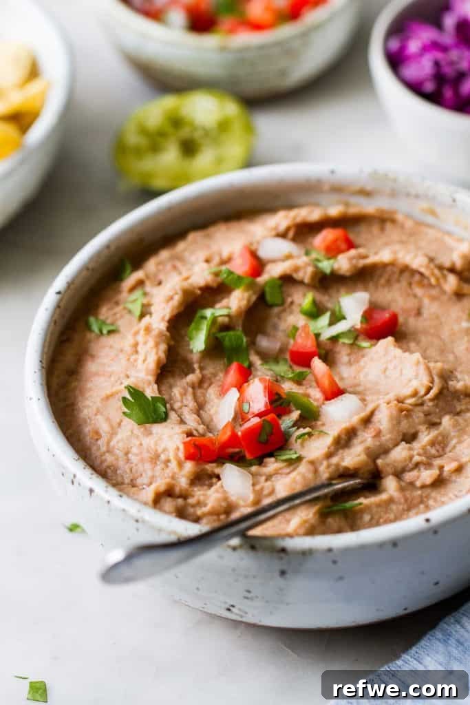 21 Amazing Meals from a Single Can of Beans 13 A ceramic bowl filled with homemade refried beans, garnished with fresh tomatoes and onions