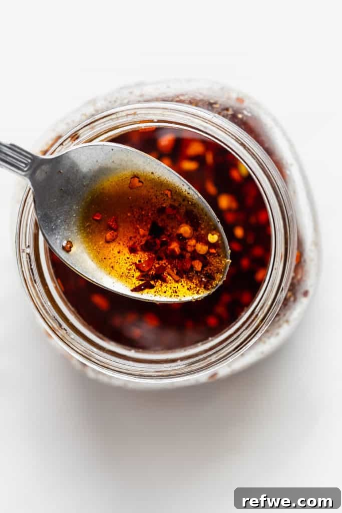 Plant-Based Dan Dan Delight 5 A spoon drizzling homemade chili oil into a bowl, showcasing its rich texture.