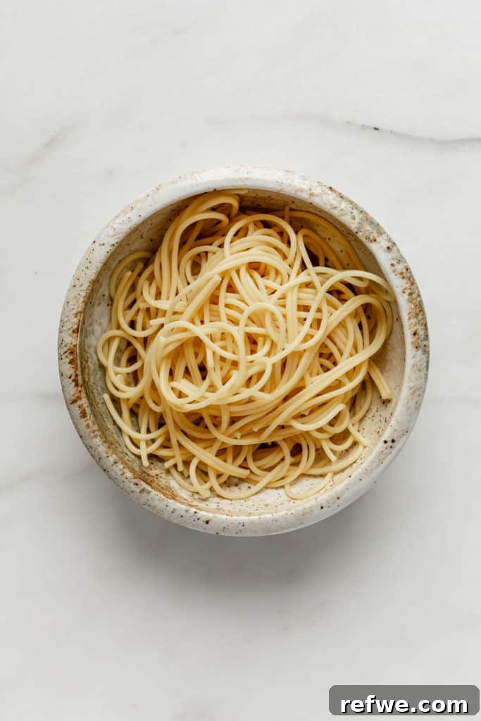 Plant-Based Dan Dan Delight 6 Cooked spaghetti noodles resting in a white ceramic bowl, ready for sauce and toppings.