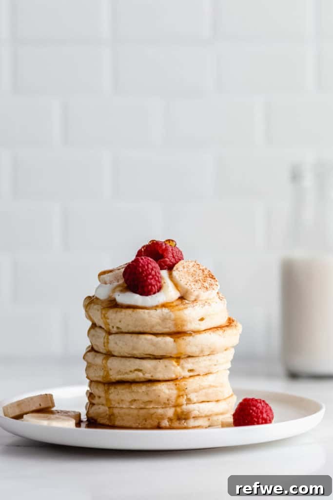 A vibrant stack of vegan oatmeal pancakes adorned with fresh raspberries and sliced bananas, showcasing a delicious topping idea.
