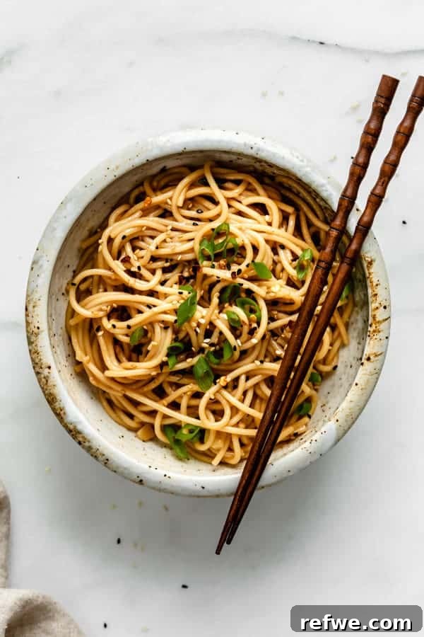 A top-down view of a bowl filled with golden Asian spaghetti, generously topped with vibrant green onions, ready to be enjoyed.