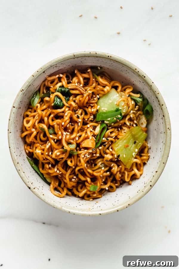 A generous serving of Ramen noodle stir fry nestled in a vibrant blue ceramic bowl, garnished with a sprinkle of sesame seeds for texture and flavor.