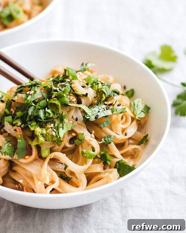 A close-up of a bowl of Life-Changing Peanut Butter Noodles, showing the thick, creamy sauce coating the noodles, garnished with crushed peanuts.