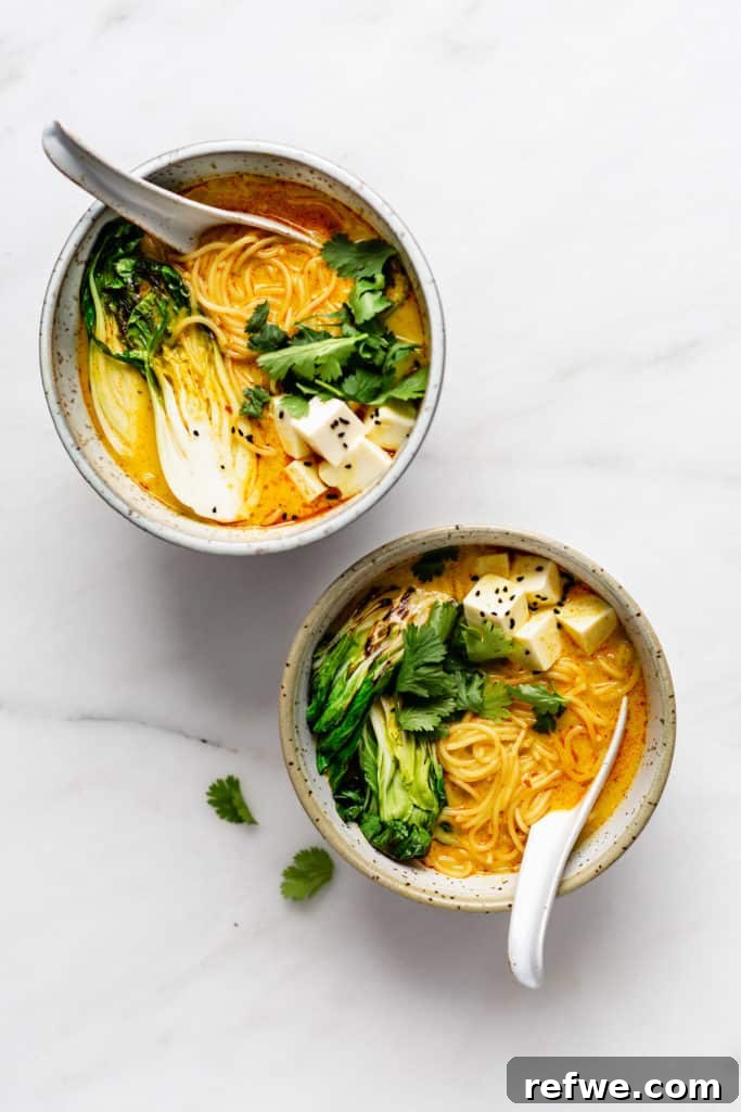 Effortless Vegetarian Laksa 2 Two steaming bowls of vibrant vegetarian laksa, garnished with fresh herbs, arranged artfully on a marble board.