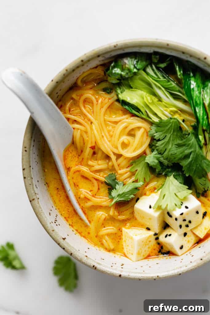 Effortless Vegetarian Laksa 4 A close-up shot of a bowl filled with laska soup, featuring perfectly cooked noodles, vibrant green bok choy, and cubes of tofu submerged in the creamy broth.