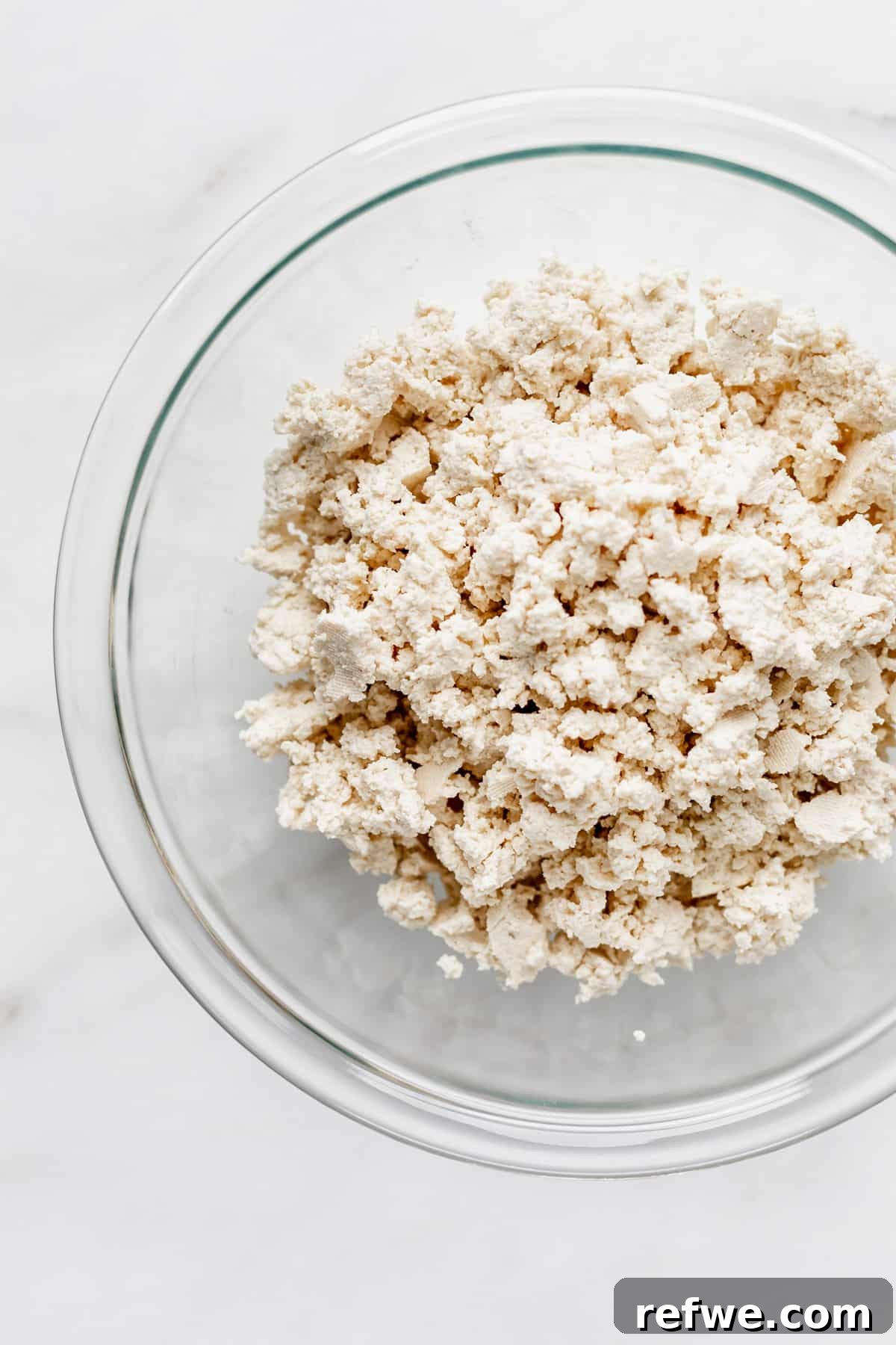 Next-Level Tofu Scramble 3 Crumbled firm tofu in a clear glass mixing bowl, showcasing its readiness for scrambling.