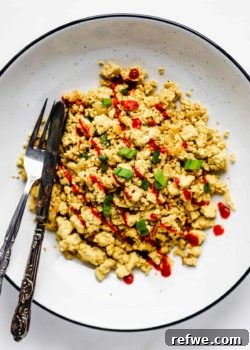 scrambled tofu topped with sliced green onions and sriracha in a large white bowl with a black rim