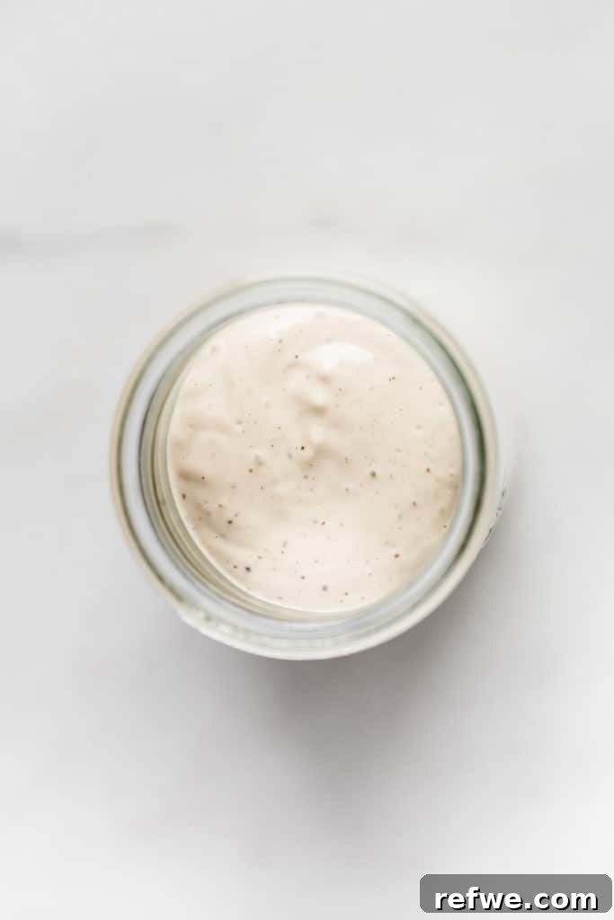 The Ultimate Vegan Caesar Dressing 3 A top-down view of a glass jar filled with luscious, creamy vegan Caesar salad dressing, garnished with fresh herbs.